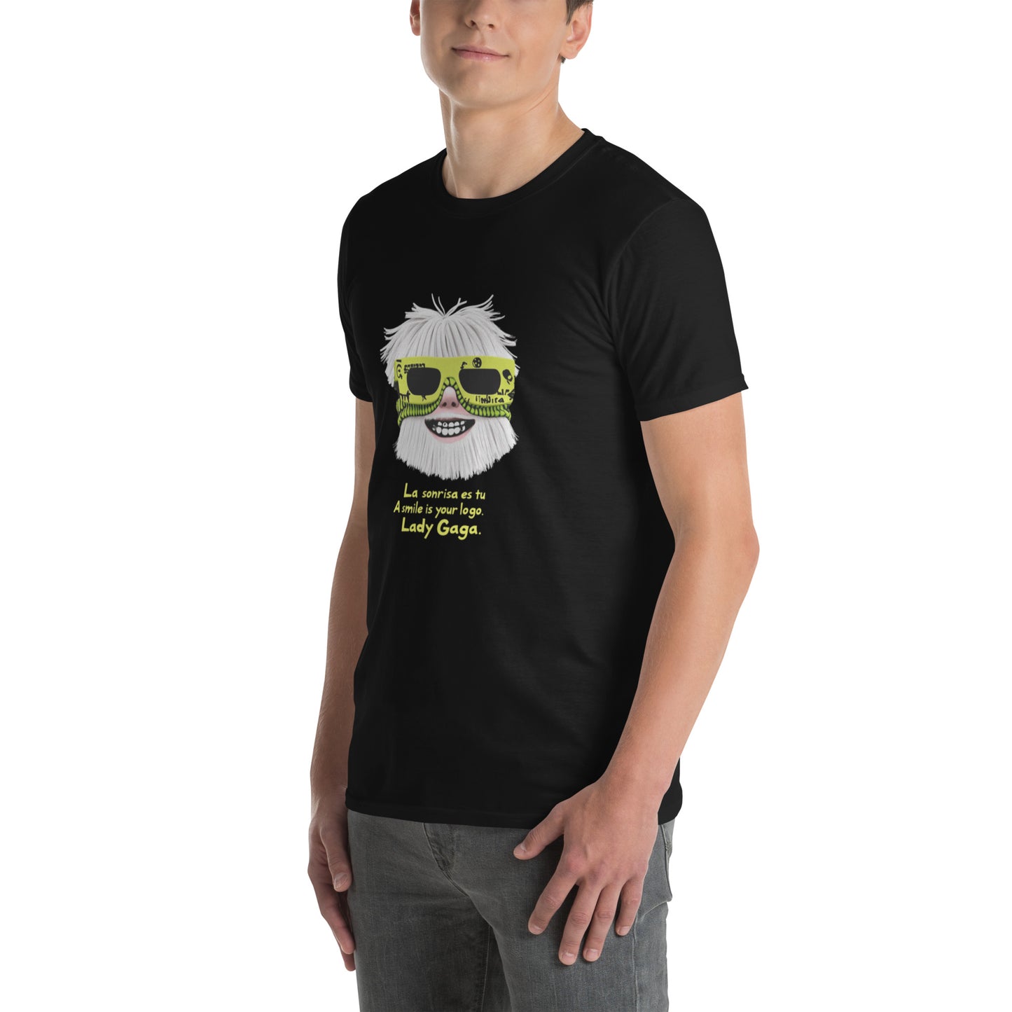 Male model wearing black T-shirt — front print: stylized face with white hair and neon sunglasses, text La sonrisa es tu / A smile is your logo. Lady Gaga.