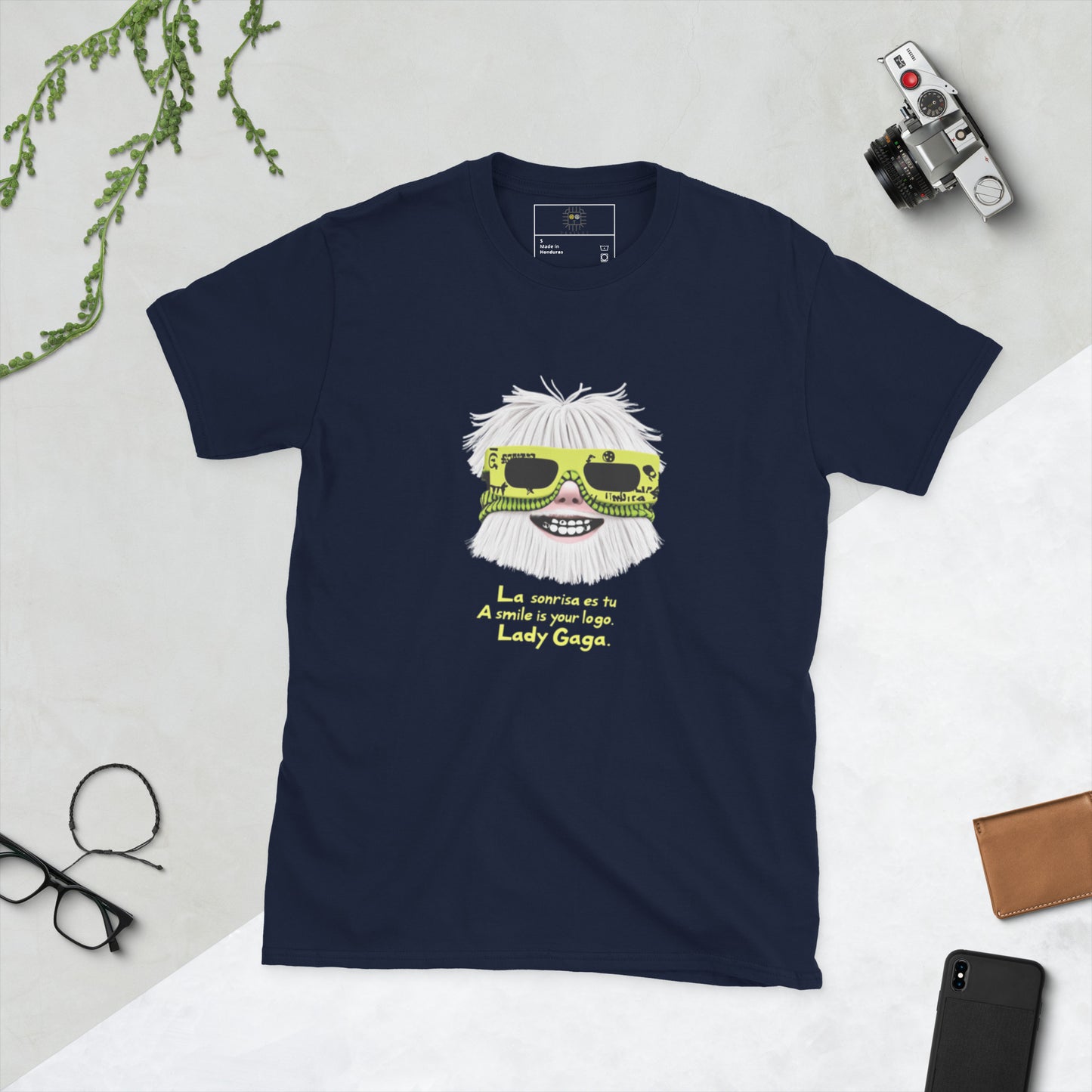 Navy blue unisex T-shirt – front print: stylized face with white hair and neon yellow sunglasses, text “La sonrisa es tu / A smile is your logo. – Lady Gaga.”