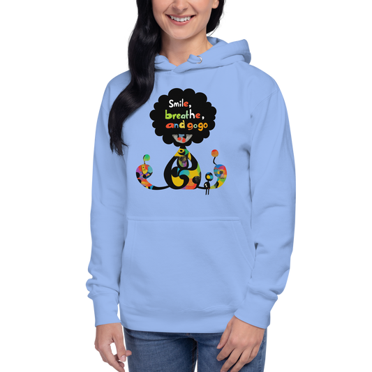 Woman wearing a light blue unisex hoodie featuring a colorful Smile, Breathe, Repeat illustration with kawaii-inspired characters and vibrant graphic details.