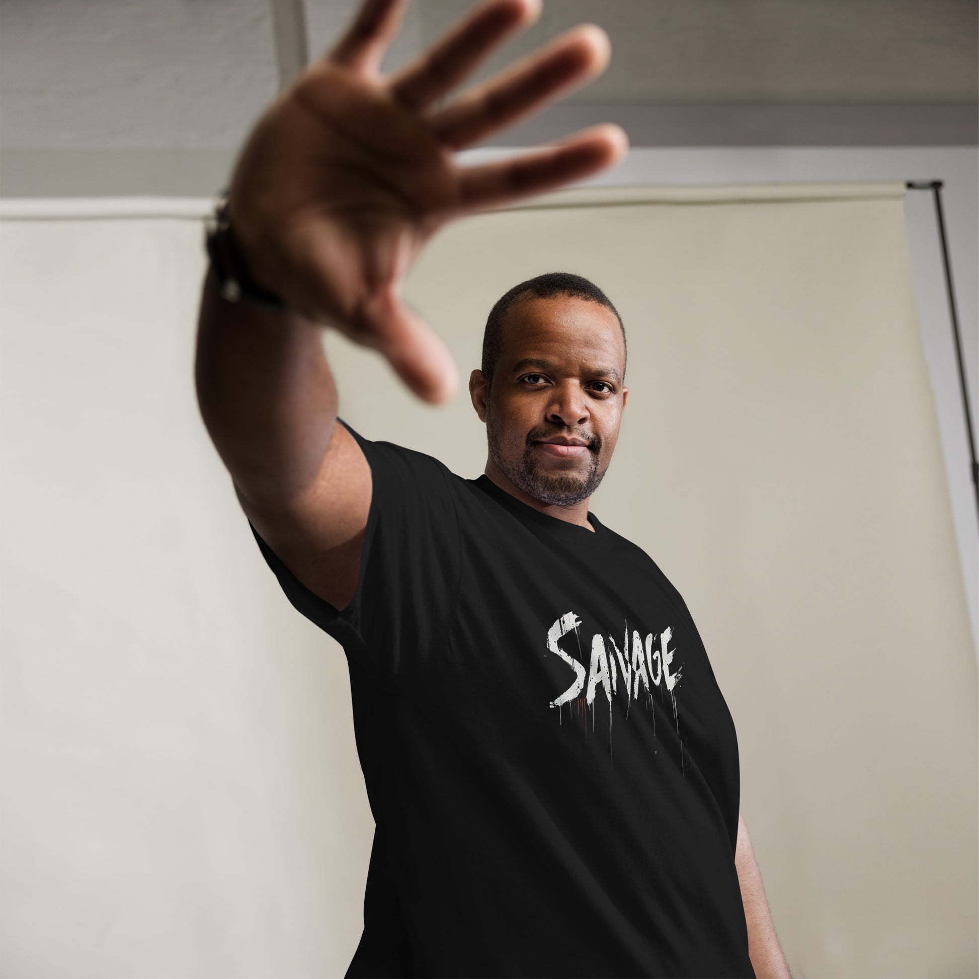 Male model: Man wearing black Savage t-shirt with bold white graffiti-style text, posing in confident streetwear style.