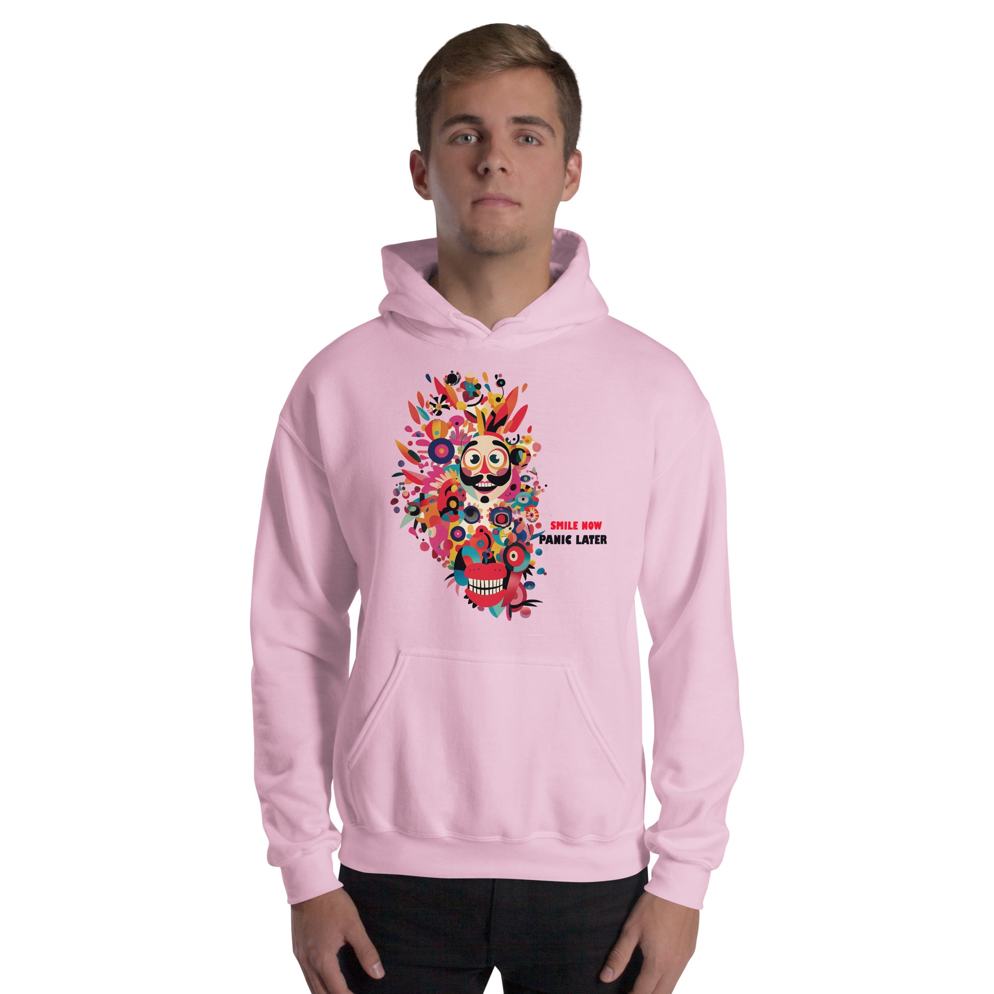 Man wearing a pink unisex hoodie featuring a colorful Smile Now Panic Later graphic with a playful character, floral elements, and vibrant pop art details.