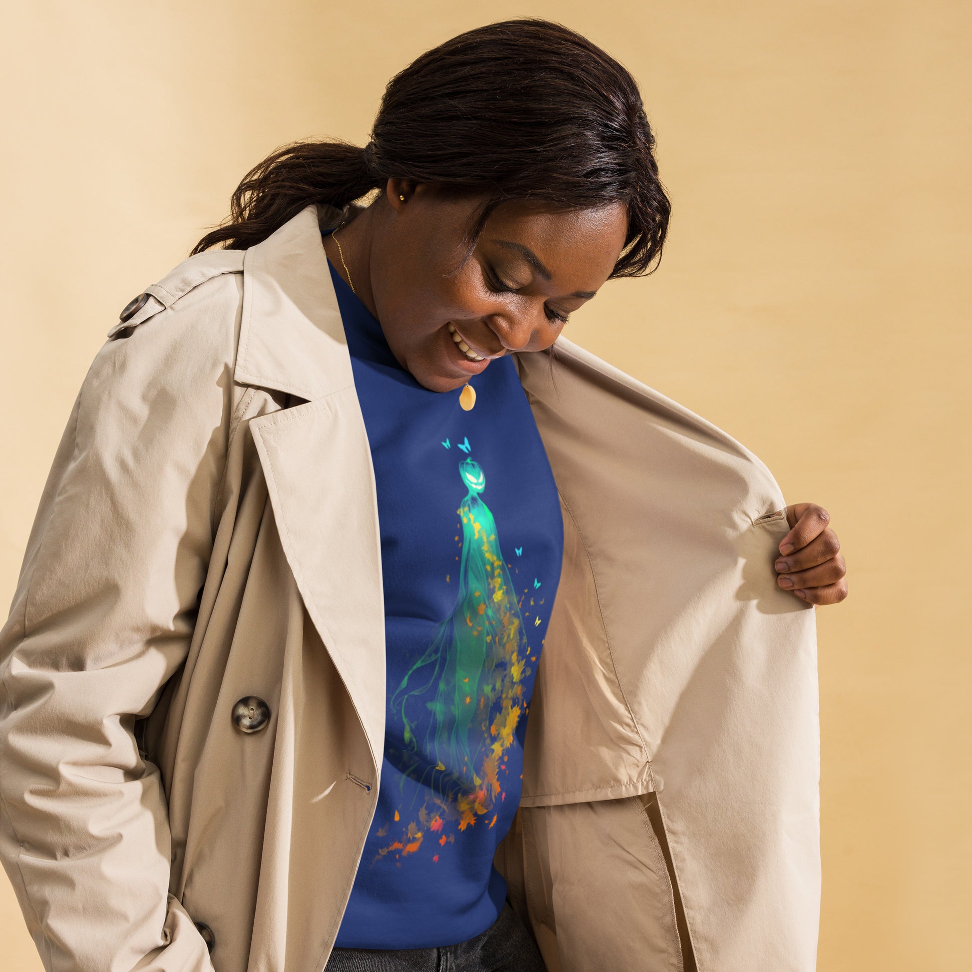 Studio model in beige coat looking at blue sweatshirt with pumpkin spirit and autumn leaves Halloween design.